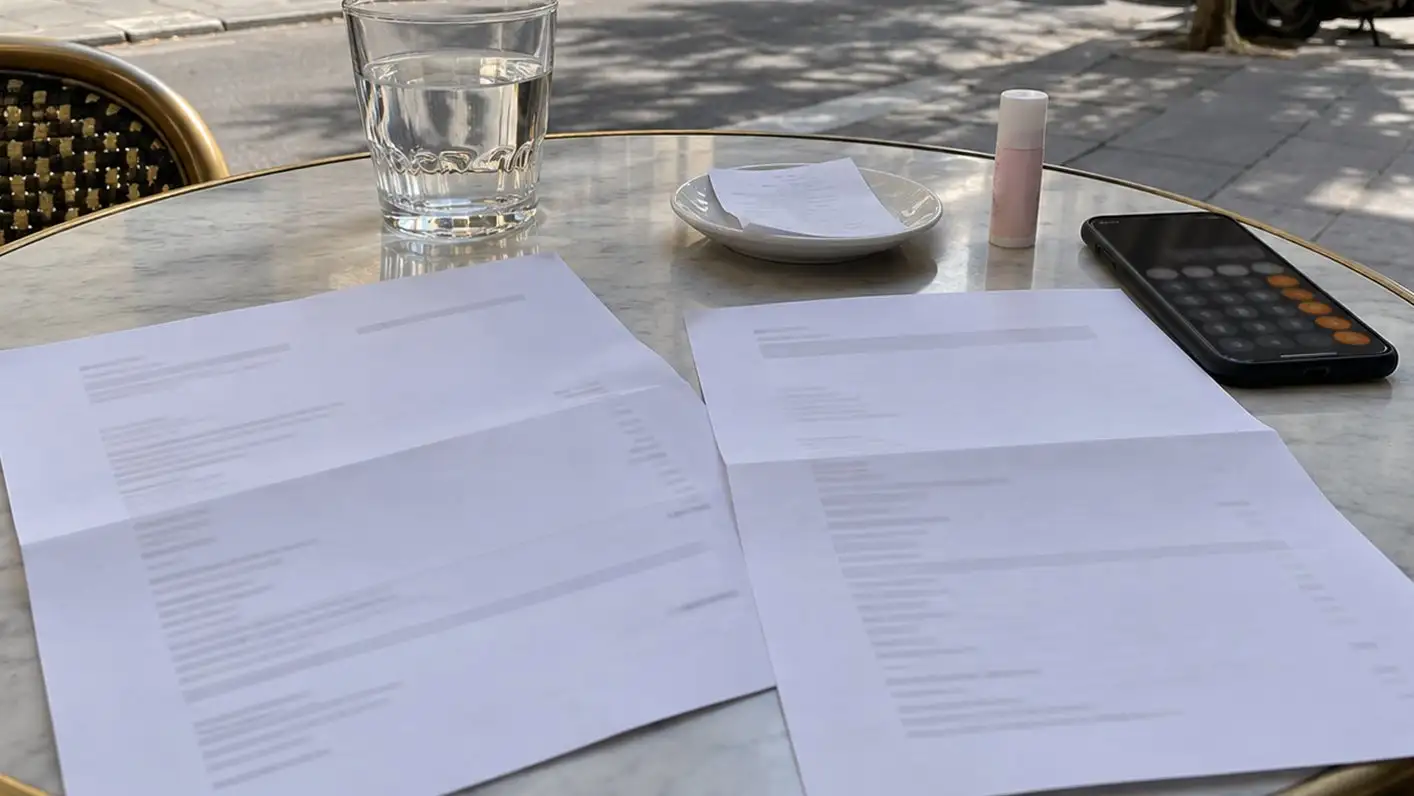 Two printed clinic quotes on a café terrace table with a phone calculator and a lip balm.
